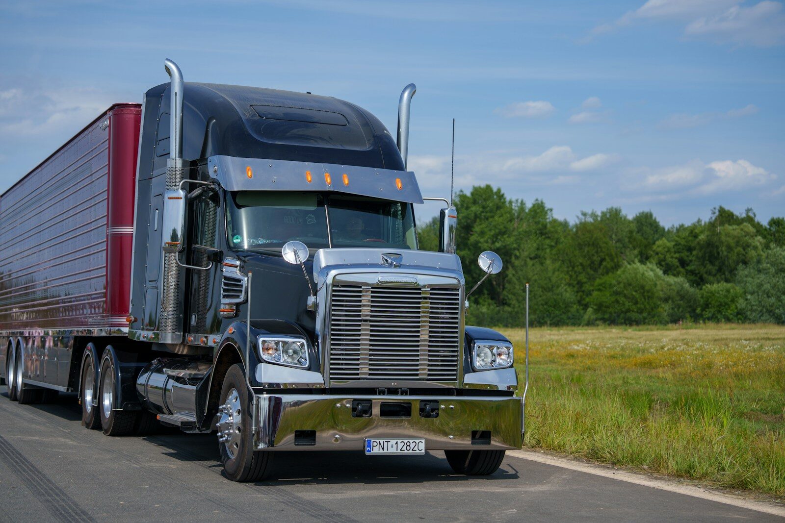 A black semi-truck drives down a rural road.